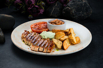 Fried chicken fillet with rustic potato wedges, beans, tomatoes and sauce in plate.