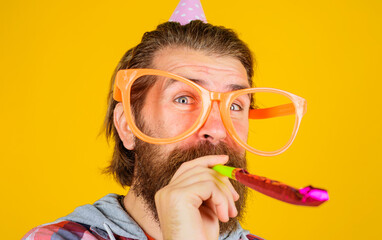 Happy birthday. Bearded man in birthday hat and big glasses blowing party whistle. Handsome man in...