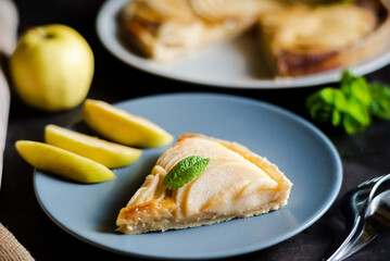 Piece of apple French pie on blue plate looks appetizing and surprisingly fresh. Thin slices of juicy apples and crispy puff pastry covered with sweet brown sugar create attractive dessert.  