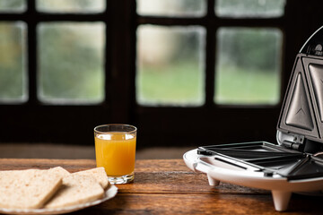 sandwich maker and a glass of juice on the background of an old-fashioned window. Preparing a quick morning breakfast, snack.