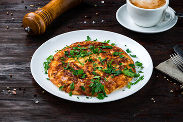 Fried omelet with sausages, herbs and a cup of coffee.