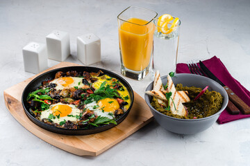 Fried eggs with bacon, onion, mushrooms, zucchini, herbs and green snack with bread and glass of juice for breakfast.
