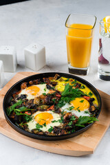Fried eggs with bacon, onion, mushrooms, zucchini, herbs and glass of juice for breakfast.