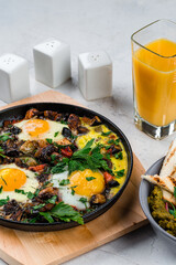Fried eggs with bacon, onion, mushrooms, zucchini, herbs and green snack with bread and glass of juice.