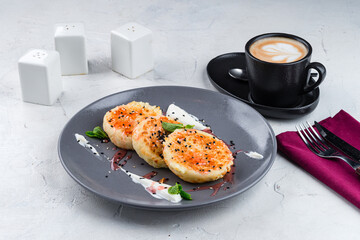 Cheese pancakes with jam, sour cream, sesame seeds, mint and cup of coffee.