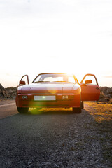Vertical photo of the front of a vintage red sports car with doors open on a mountain road at...