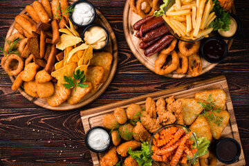Fastfood fried chicken legs and fillet, crispy onion rings, cheese balls and sticks, squid rings, sausages, french fries, garlic croutons, nachos, sauces and greens.