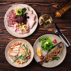 Lunch grilled white fish with tomato, lemon and herbs with Caesar salad and plate of meat.
