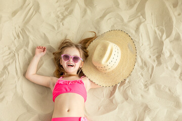 Happy little girl lying on a sandy beach and sunbathe in the sun