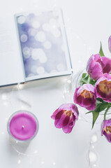 A bouquet of tulips and a magenta candle with lights and a notepad closeup.