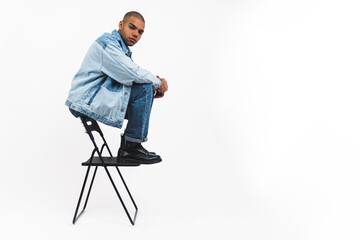 full shot of a young man in denim sitting on the back of the chair, copy space, studio shot. High quality photo