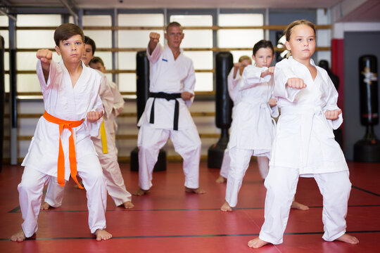 Young boys and girls in kimono doing kata moves with their trainer in gym.