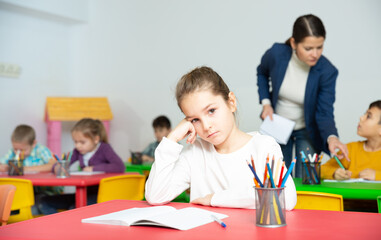 Portrait of tired schoolgirl sitting at pupils desk at lesson in primary school