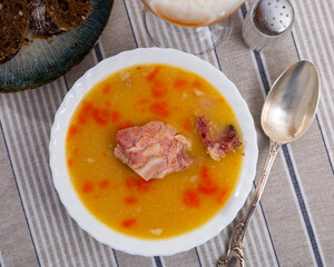 Pour steaming pea soup with smoked meats into round clay plate