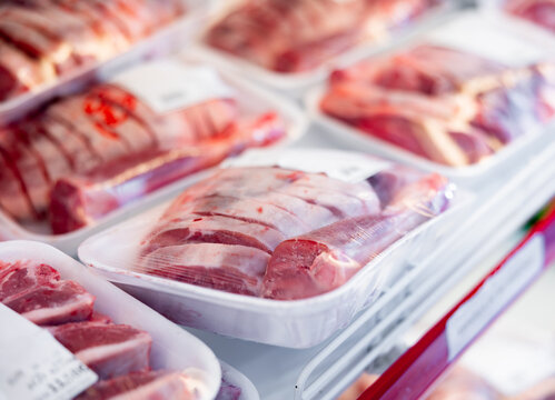 Pieces of fresh raw lamb packed in plastic trays wrapped in film with labels offered for sale in butcher shop