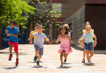 Fototapeta premium Team of positive kids running in race in the street and laughing outdoors