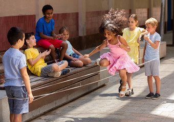 Happy little girl jumping game by rubber band with friends on the street