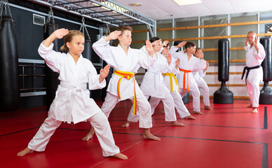 Karate kids in kimono performing kata moves with their teacher in gym during group training.