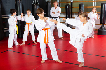 Preteen kids working in pair, mastering kicks in karate class with trainer
