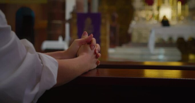 Woman folded her hands in prayer at a pew in church. Female hands close-up slow-motion.