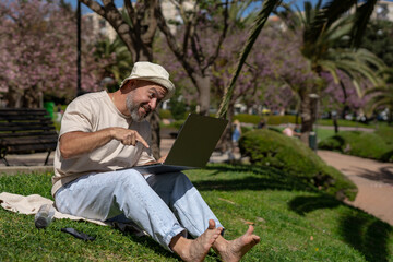 digital rocker funny bearded male freelancer with bare feet works on laptop while sitting on green...