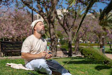 Obraz premium bearded male freelancer in the park with a laptop drinks water from a bottle while sitting on the grass with bare feet