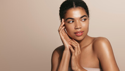 Beauty and wellbeing. Beautiful Black woman with clear, glowing skin and shiny body after spa and shower effect, using moisturizing creams and hydration serums, standing over brown background