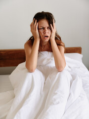 Woman sadness sits on the bed in the bedroom and covers her body with a blanket, early awakening, sleepy appearance, hangover, fatigue and depression, emotional burnout