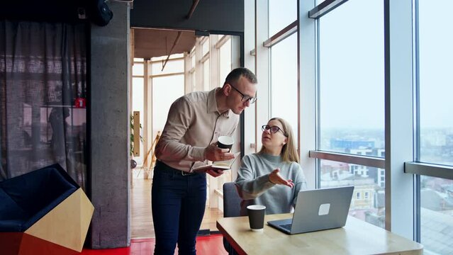 Long-haired lady points at laptop in front of her. Female colleague explaining some issues to her male workmate.
