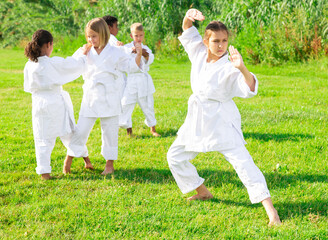 Hispanic girl in kimono practicing karate with friends in park. High quality photo