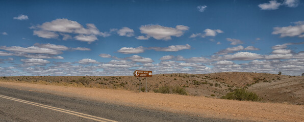 Sign to Mundi Mundi lookout on Wilangee Road, near Silverton, New South Wales, Australia. Desert landscape. Fluffy white clouds in deep blue sky