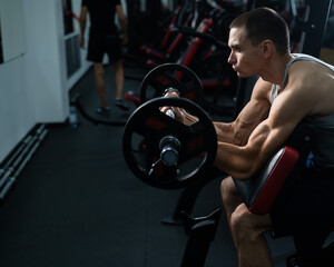 Man doing EZ barbell bicep exercises on Scott bench. 