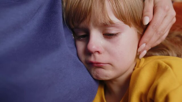 Close-up portrait of upset child little girl kid crying with tears flowing down on her cheek, toddler lies on mother at home. Mom hugs, embrace, takes pity on her daughter. Quarrel, bullying at school