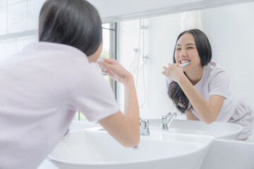 Obraz premium Happy Asian woman brushing her teeth with a toothbrush in the bathroom in bright morning.