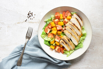 Healthy food grilled chicken vegetable pumpkin lettuce tomato salad in bowl on white wood table.