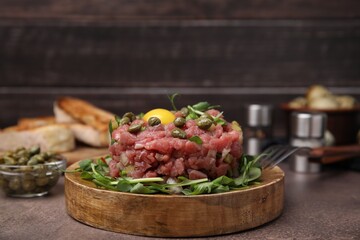 Tasty beef steak tartare served with yolk, capers and microgreens on brown table