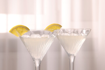 Elegant martini glasses with fresh cocktail and lemon slices near curtain