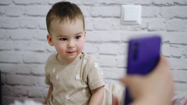 Beautiful toddler boy with cute rosy cheeks is focused on the phone. Parent holds a gadget for kid and he is mesmerized by the view.