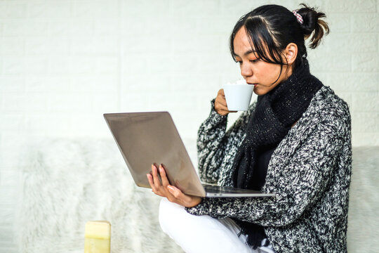 Young woman in winter clothes checking online shops for cyber monday sales at the laptop while enjoying coffee- technology woman concept for alternative office freelance. Working in winter. 