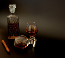 Cuban cigar, crystal decanter and two glasses of whiskey on a black background.