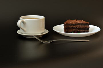 A plate with a piece of mint leaf chocolate puff cake, a fork and a cup of hot black coffee on a saucer on a black background on a black background.