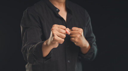 Fototapeta premium A man in a black shirt raised his fists while standing against a black background