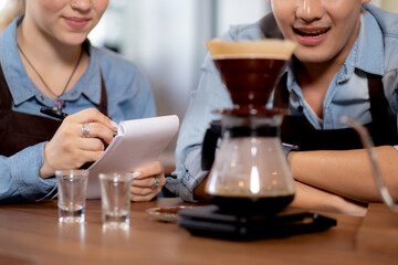 Young man and woman learning making coffee with barista while pouring coffee at cafe, group people training drip coffee with entrepreneur while writing note with coffeeshop, small business or SME.