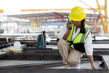 Young woman engineer using radio command with worker in construction site, architect or contractor speak to radio for control and planning development structure at precast factory, industrial concept.