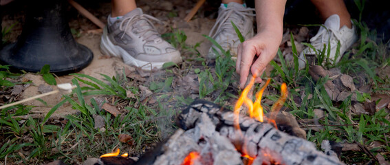 Closeup hands of friends grilling marshmallow on bonfire in camping, picnic in campfire, group friends party and relax together in vacations.