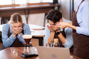 Young man and woman learning making coffee and sniff bean with barista while laptop on desk at cafe, group people training drip coffee with entrepreneur, small business or SME.