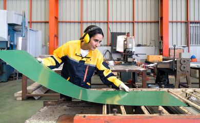 Young female hispanic labor dressed in polyester jacket uniform and ear muff working in metal sheet...