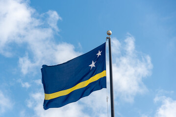 Flag of Curacao waving on a flagpole with a blue sky in the background. Netherlands Antilles.