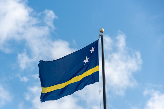 Flag of Curacao waving on a flagpole with a blue sky in the background. Netherlands Antilles. - Powered by Adobe