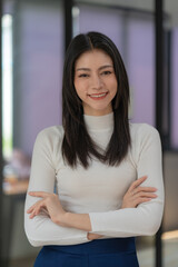 Attractive Asian businesswoman standing with crossed arms and looking at camera in office confident and happy with business success
